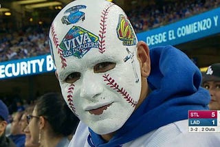 A Dodger fan at a Dodger game with his face painted as a baseball and “Viva Los Dodgers” printed on his forehead.