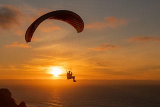 A man paragliding over a sea at sunset