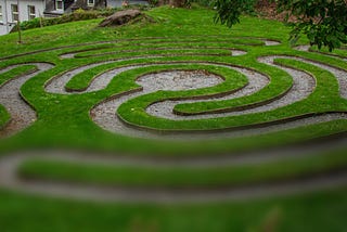 A grassy labyrinth shown in a partially-loaded photo that is clear on the top and blurry at the bottom.