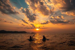 two person riding two kayaks on the surface of the sea and enjoying sunrise