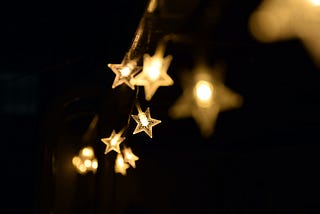 Yellow fairy lights in the shape of stars hanging against a dark sky.