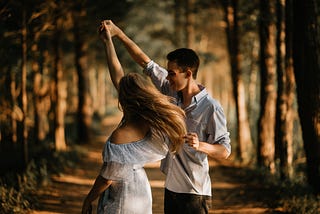 A girl and a boy expressing love as they joyfully dance together amidst nature’s beauty.