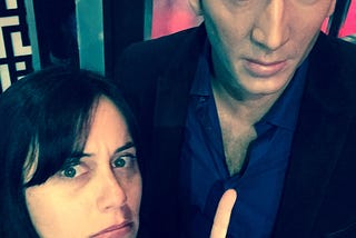 Photo of Kona next to a life-size wax figure of Nicolas Cage. She is pointing at him with an expression that says, “I’m Pretty Sure Nicolas Cage is My Gynecologist.”