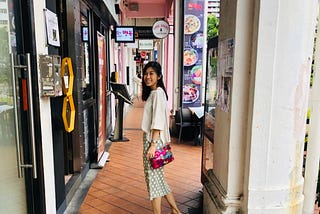 A lady standing in the middle of an alley, turning back to face the camera with a smile on her face.