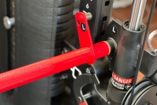 A close up on one side of a bright red Smith bar attached to a black functional trainer.