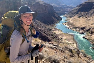 Woman smiling, wearing a backpacking backpack with a view of the Colorado River inside the Grand Canyon