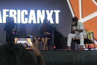 Speakers on an AfricaNXT stage; a young woman takes a photo of them with her mobile phone.