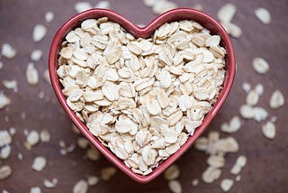 A close up of red heart shaped bowl filled with rolled oats.