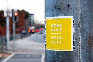 an image of a yellow poster that says “more love” “less fear” on a wall