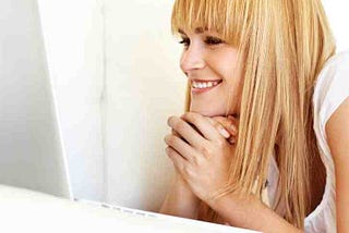 Headshot of Pretty, young blonde girl smiling at screen with hands claspped against white background.