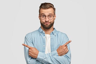 Hesitant and clueless man crosses hands over chest, indicates with index fingers in different sides or directions, can’t make choice between two different career choices available to him