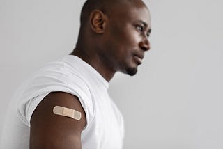 Close-up shot of a man with his shoulder prominently displayed with a band-aid on it.