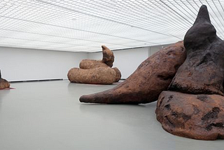 A large white room in an art gallery with three enormous sculptures in the shape of turds