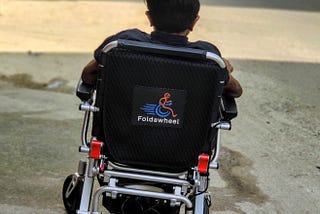 A person in a wheelchair with his back facing the camera. He is on the road, moving ahead in life