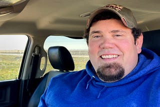 A portrait of a man in a hat with a blue sweater