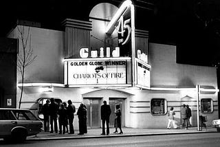 People outside the Guild 45th Theater in Seattle, circa 1982. It’s at night with several people standing in line to be tickets under a neon marquee for the film “Chariots of Fire.”