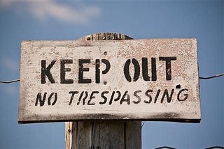 A sign board on a fence which says, “Keep Out No Trespassing”.