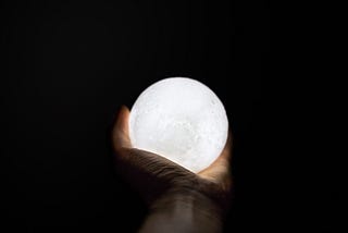 A hand holding a glowing orb against a black background.
