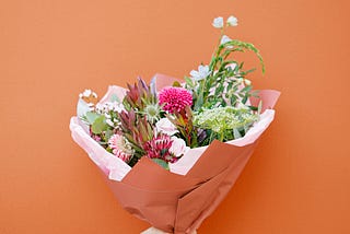 Hand and arm holding a bouquet of flowers on an orange background.