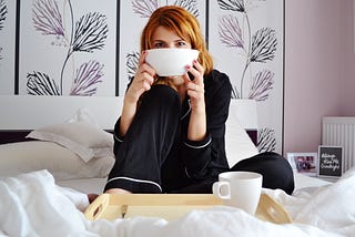 Woman in pyjamas sitting on bed with tea and cereal bowl