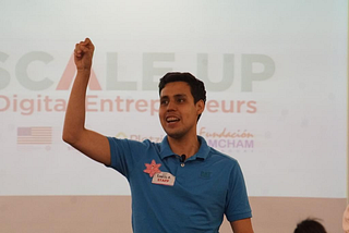 A young adult in a polo stands with his fist in the air.