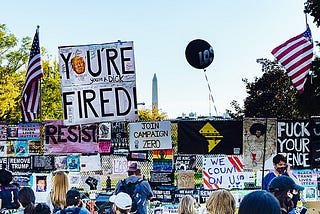Anti-Trump activists with signs in a photo from 2020 in Washington, DC, saying “You’re Fired,” “Resist,” and “Fuck Your Fence.”