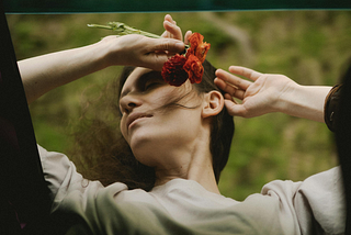 An image of a woman holding a flower, her hair flowing in the breeze, embodying well-being and liberation in the present moment.