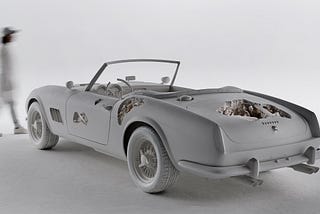 A recreation of a 1961 Ferrari convertible — with a twist. Portions of the car are cratered out or have gashes, both on its exterior and within the car’s upholstery and dashboard. Beautiful mineral crystals emerge from those damaged cavities.