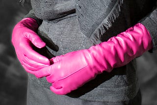 Torso of woman wearing black with elbow length pink leather gloves clasped in fron-nt of her.