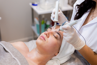 A young woman lies on a beautician’s table during a microcurrent treatment procedure
