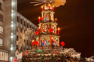 A vibrant Christmas Pyramid at Hannover’s Kröpke, illuminated with candles, festive decorations, and figures, surrounded by a bustling holiday market. The scene evokes the timeless charm of Advent traditions. Photo by Jay Siegmann.