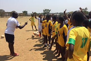 Ashoka Fellow Elvis Nshimba talking to a group of sports players in yellow jerseys.