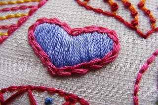 Close up of embroidered heart in blue and pink stitching.