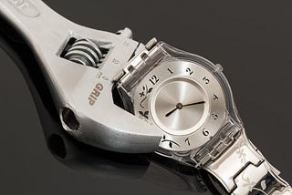 A Spammer Tool Positioned On A Silver Wristwatch Against A Grey Backdrop.