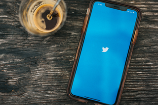 A phone with the Twitter Bird logo and a nearly empty coffee cup.