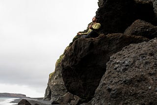 A woman sitting on a rock above an ocean, practicing meditation.