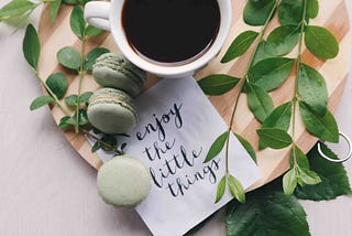 A cup of coffee and macarons arranged on a wooden platter