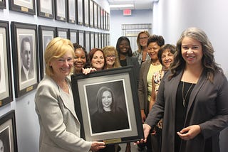 Sarah Eubanks holds official portrait of her daughter, Rachael with SOM employees in the Hall of Treasurers.