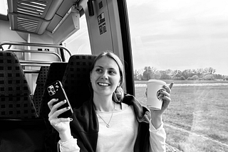 woman smiling sitting on the train holding a coffee cup and phone in the other hand