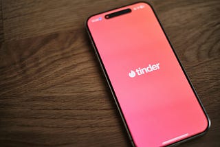 Smartphone on wooden table showing Tinder splash screen