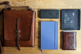 A picture of my satchel, notebook, ereader, pocket, and battery