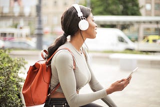 Woman with headphones on audio journaling with her phone while sitting down outside