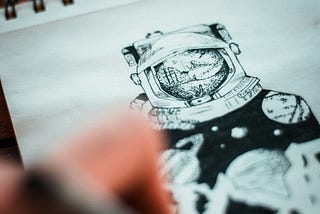 Photo of someone drawing an astronaut on a sheet of paper.
