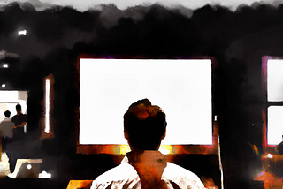 A man sitting in front of a large blank computer screen in a dark office.