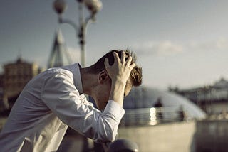 A man sits outside in a city, clutching his head