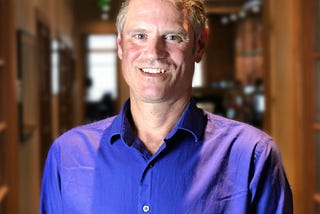 Headshot of Robin Murphy in his office, Seattle, WA, in a purple button down shirt