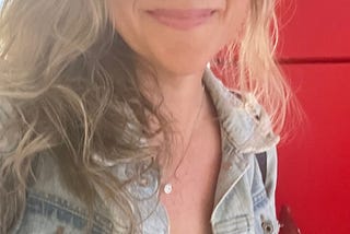 author blonde hair, jean jacket, red wall