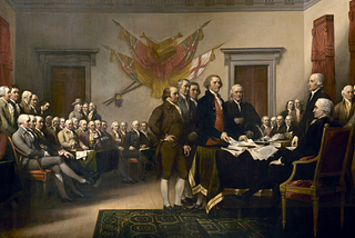 Painting called “Declaration of Independence” of an 18th century scene. Five white men stand in a fancy hall to present a seated man with a paper. Two rows of mostly seated men look on.