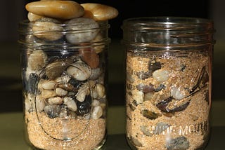 Two jars. One overloaded with sand coming first and one filled with bigger rocks coming first then covered with sand.
