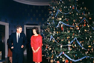 President John F. Kennedy and First Lady Jacqueline Kennedy standing beside the Blue Room Christmas tree in 1961, decorated with Nutcracker-themed ornaments.